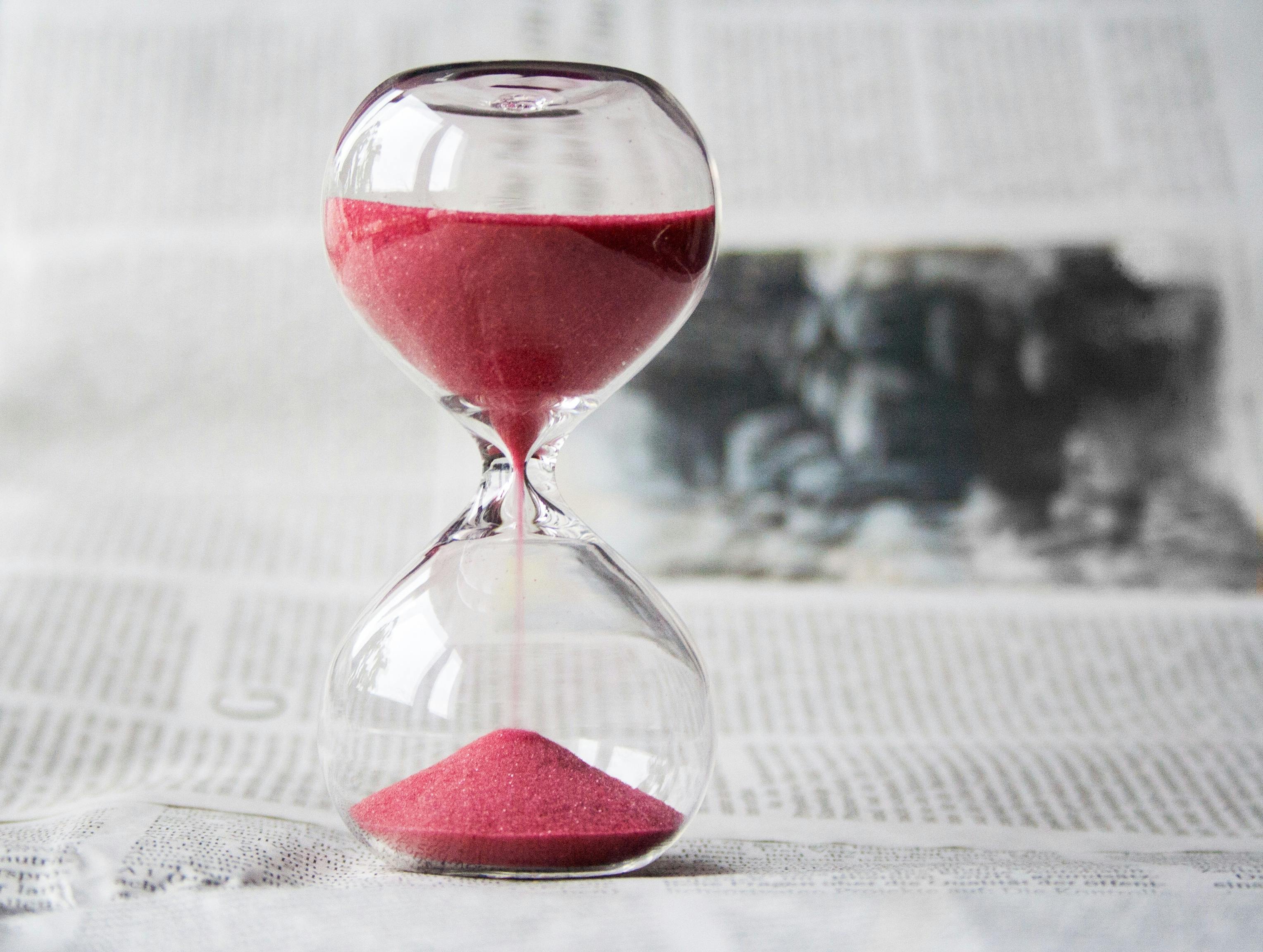 Hourglass with red sand on top of newspaper