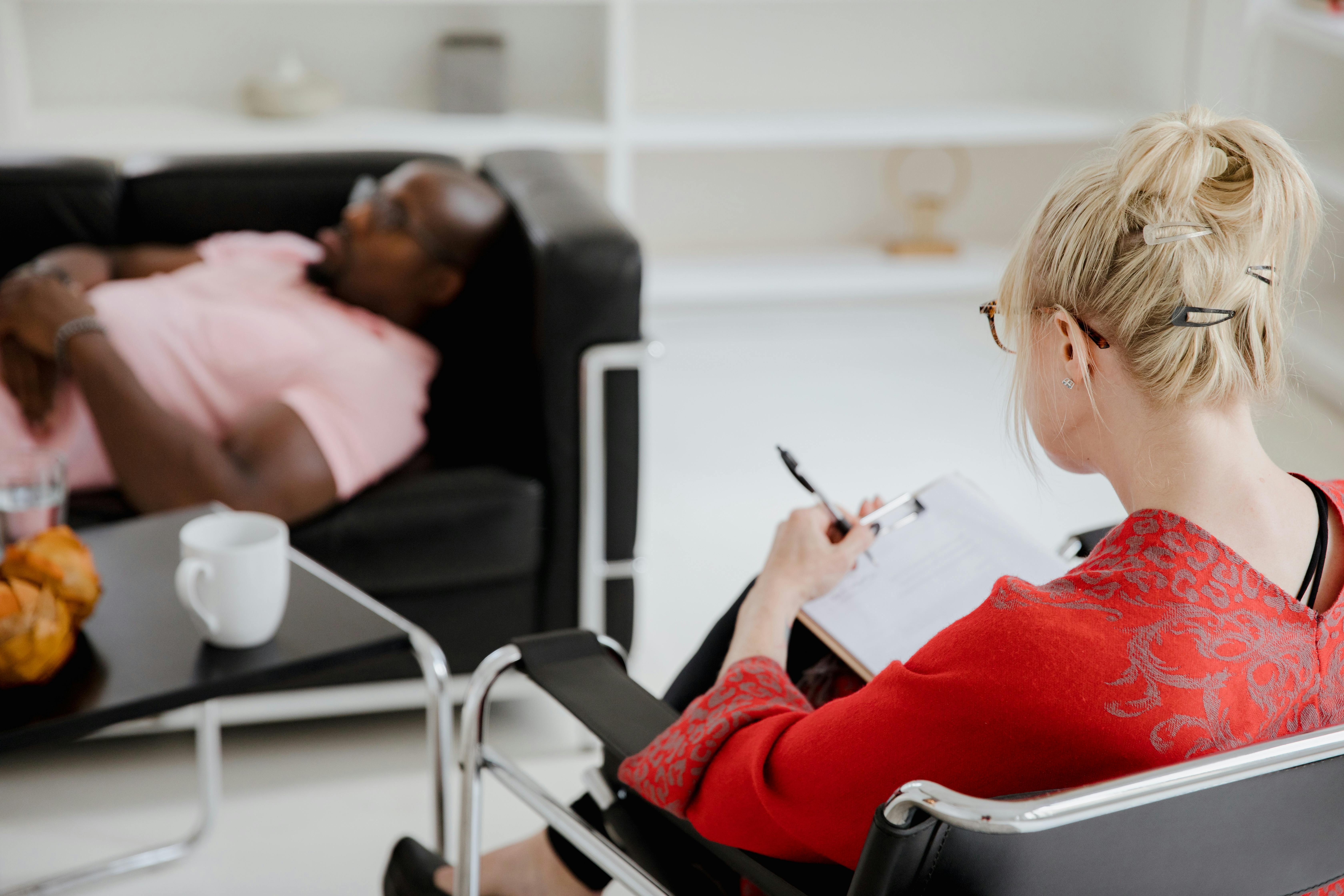 therapist taking notes with man on couch in background