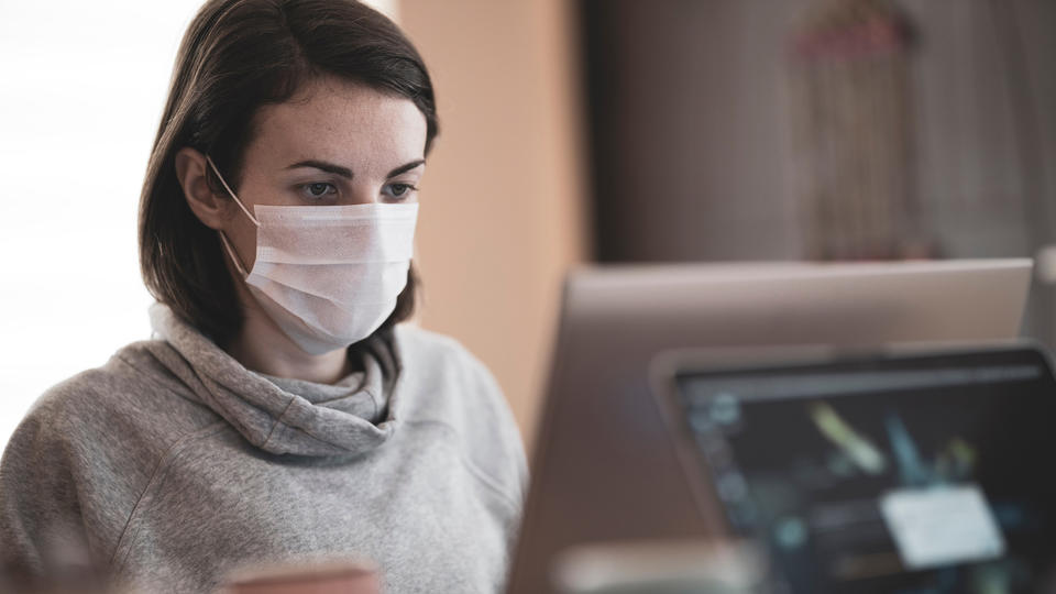 Woman wearing mask staring at computer screen