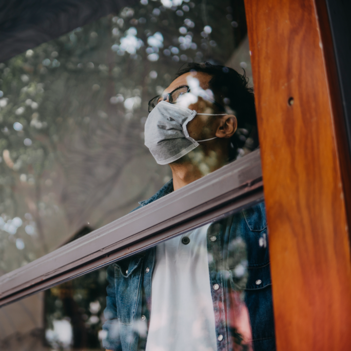 Man staring out window wearing mask
